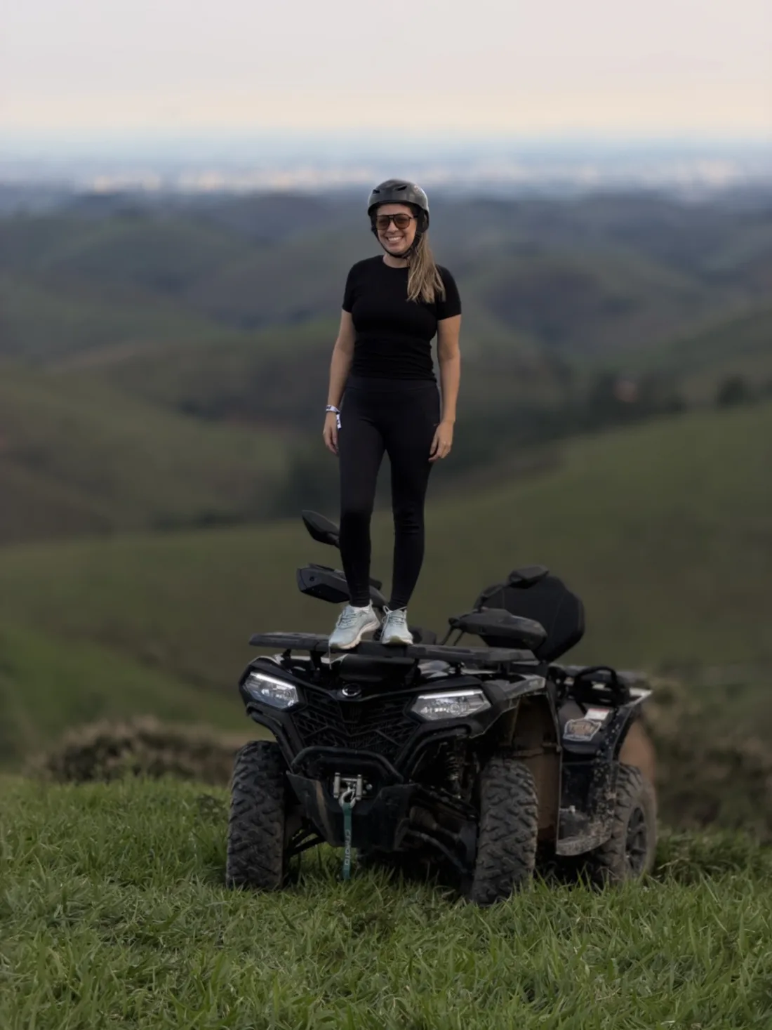 Carol em pé sobre um quadriciclo, com montanhas ao fundo